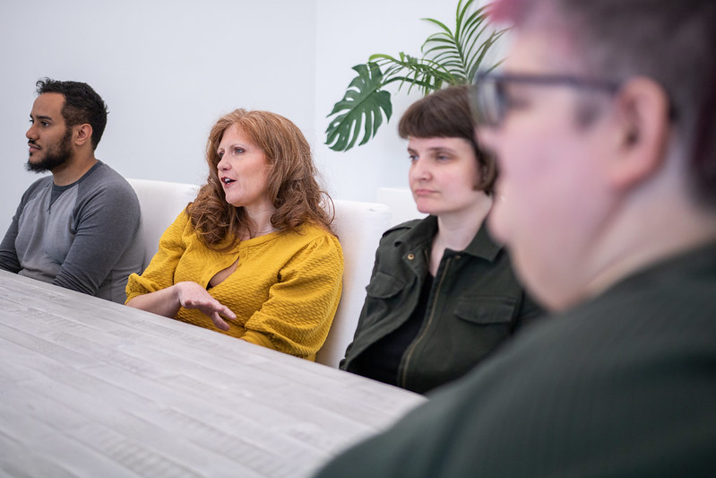A group of friends and peers gather around a long table in a homely setting.
