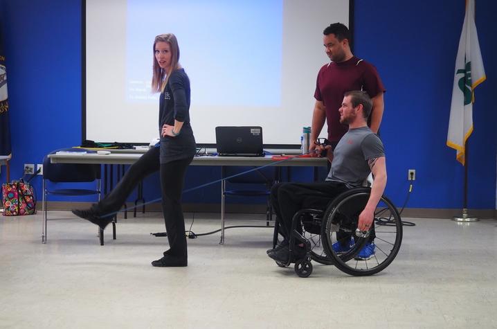 Two men, including one with prosthetics and one man using a wheelchair, exercising with a woman