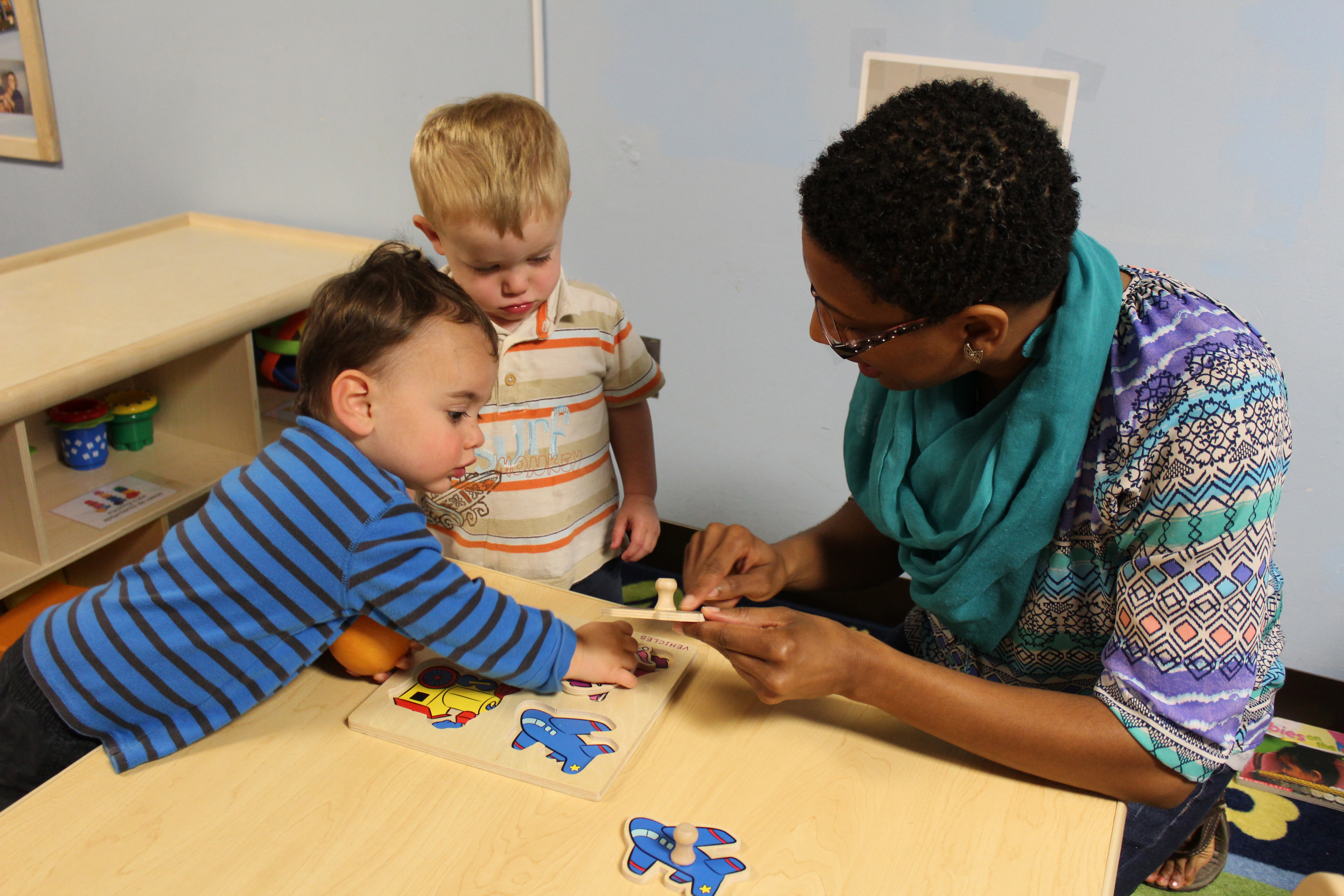 Two young preschool-aged boys working with a teacher on a puzzle.