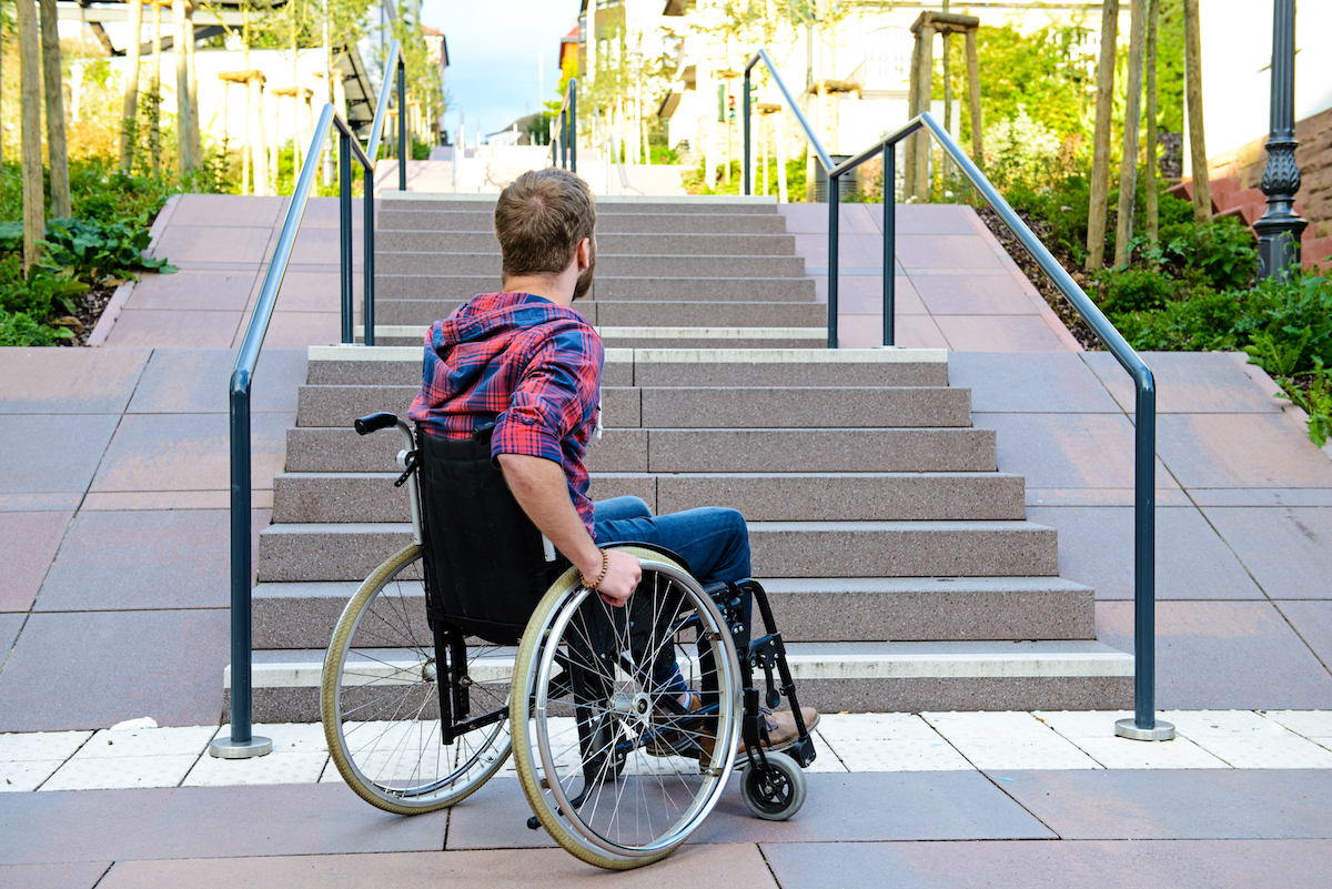 Man in a wheelchair looking up stair that are not accessible.