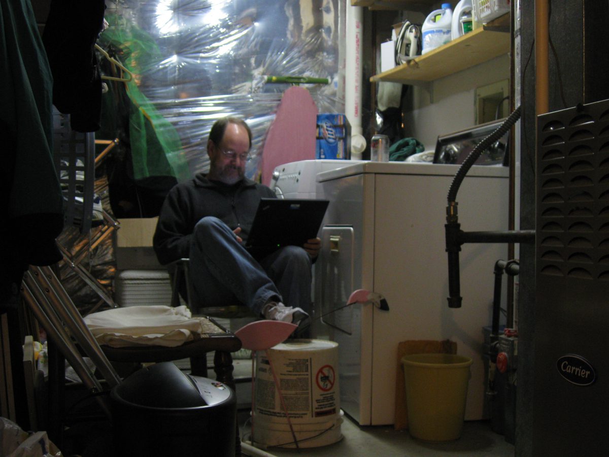 Man working on a laptop next to a washing machine.