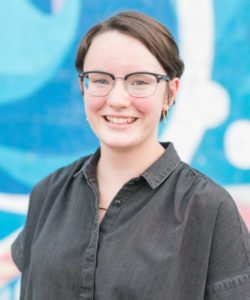 Haley wearing a black shirt smiling at the camera in front of a blue mural