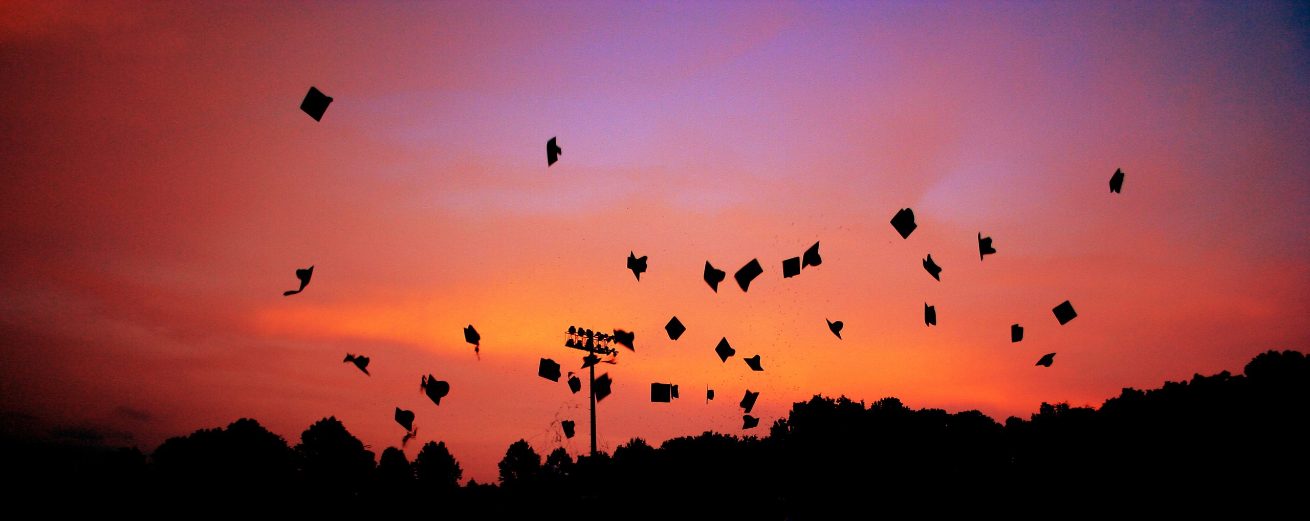 black graduation caps being thrown in the sunset sky