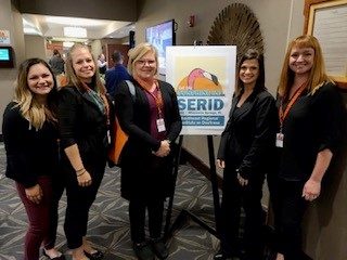 ASL Team standing in front of SERID Conference poster