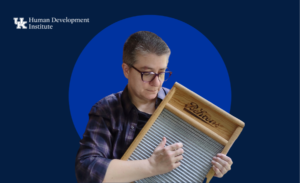 Erin Fitzgerald, a staff member of HDI is wearing a blue flannel and holding a washboard to make music. they are on a blue background with HDI's logo in the top left.