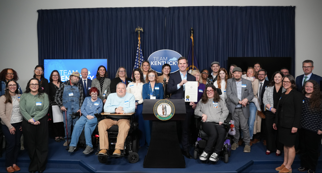 Governor Andy Beshear with a large group of people behind the podium at the signing ceremony